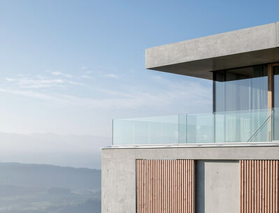 GM Railing Uni Part Sulzberg  Modernes Einfamilienhaus mit Betonfassade, großen Fenstern und Glasgeländer auf einer Anhöhe mit weitem Blick über die Landschaft.