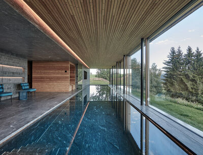 Innenansicht eines modernen, eleganten Schwimmbades mit einem großen Fenster, das einen Blick auf die umliegende Natur bietet.