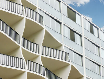 GM Toproll Parapet Magdeburg  Fassade eines modernen Wohngebäudes mit wellenförmigen Balkonen und minimalistischen Glasfronten.